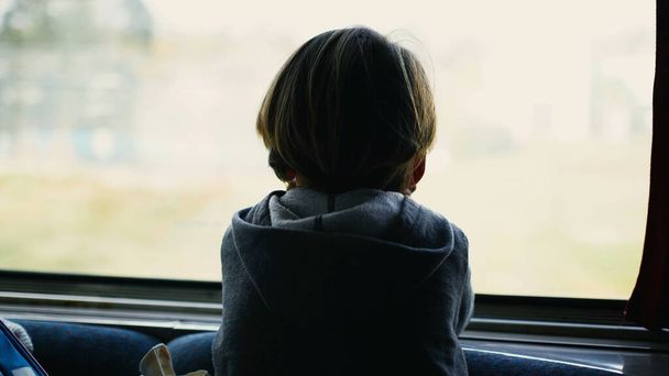 Achterkant van attent kind leunend op treinraam kijkend naar parallelle trein op spoorweg passeren in hoge snelheid. Kind op reis tijdens dagdromen - Foto, afbeelding