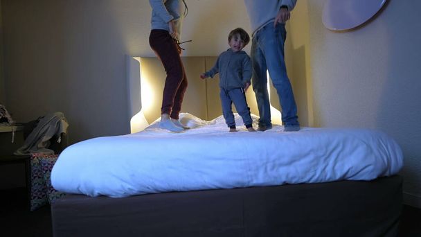 Temps de famille heureux - Les parents et l'enfant sautant sur le lit de l'hôtel - Photo, image