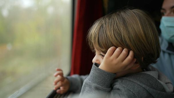 Cestující dítě cestující vlakem zírající na paralelní vlak projíždějící uvnitř vysokorychlostní dopravy. Zamyšlený malý chlapec s rukama v bradě zasnění při cestování - Fotografie, Obrázek