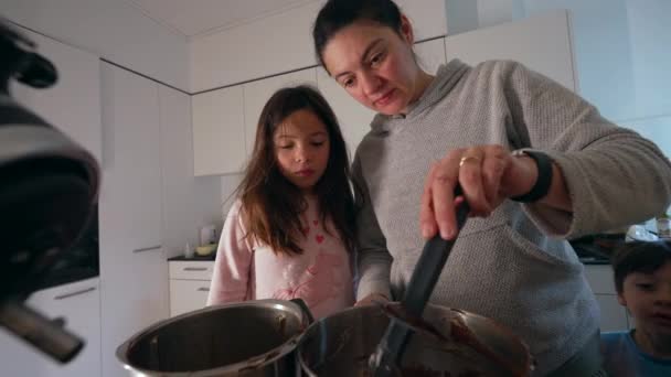 Mère préparant la nourriture à côté de sa fille tandis que son fils erre dans la cuisine, authentique scène de style de vie familial cuisine des parents tenant la spatule à la main mélangeant les ingrédients - Séquence, vidéo