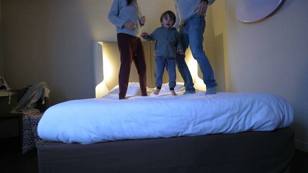 Tempo familiar feliz - pais e criança pulando na cama do hotel - Foto, Imagem