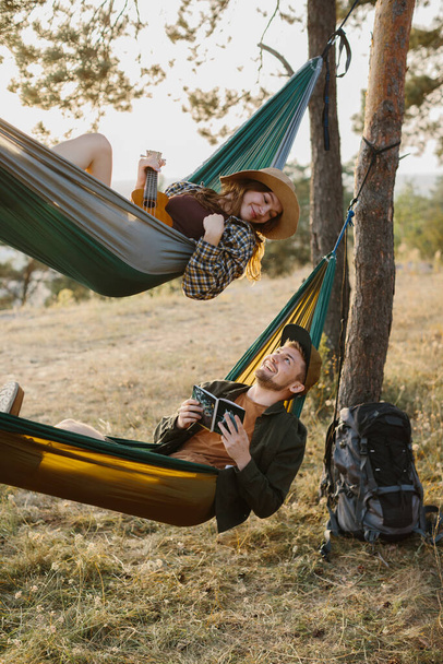 Een jongen en een meisje ontspannen in hangmatten in een dennenbos bij zonsondergang.  - Foto, afbeelding