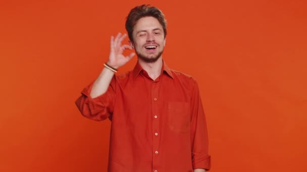 Okay. Happy Caucasian man looking approvingly at camera showing ok gesture like sign positive feedback, approve something good celebrate victory wink blink eye flirting. Young guy on orange background - Footage, Video