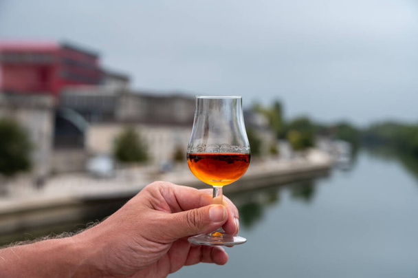 Tasting of aged in barrels cognac alcohol drink and view on old streets and houses in town Cognac, Grand Champagne, Charente, strong spirits distillation industry, France - Photo, Image