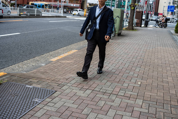Tokio, Japonsko, 31. října 2023: Podnikatel kráčí po chodníku v rušné městské oblasti - Fotografie, Obrázek