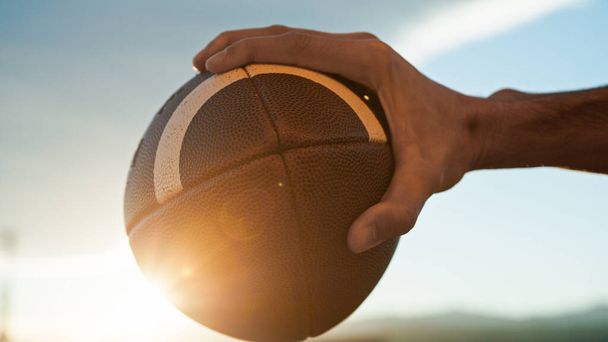 χέρι κατέχει αμερικανική μπάλα ποδοσφαίρου στο ηλιοβασίλεμα. - Φωτογραφία, εικόνα