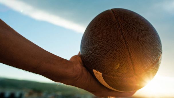 main tient ballon de football américain au coucher du soleil. - Photo, image