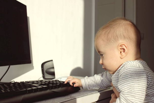 Un niño lindo está sentado en la computadora y mira con atención con admiración - Foto, Imagen