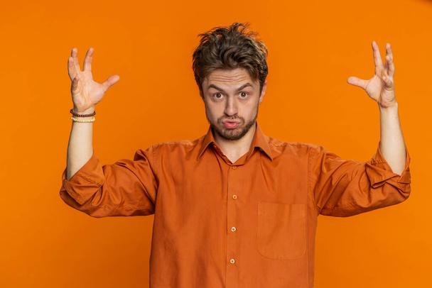 Excited amazed Caucasian man touching head and showing explosion, looking worried and shocked, celebrating success achievement, good idea, answer. Handsome guy isolated on orange background indoors - Photo, Image