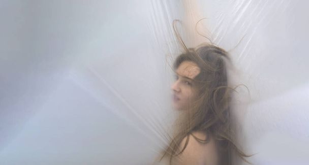 θολή, θολή εικόνα πορτρέτο του αισθησιακό νεαρή γυναίκα πειράγματα, άγρια μαλλιά στο πλαστικό φιλμ, κινείται σε έκσταση πίσω από πλαστικό φύλλο, αντίγραφο χώρο - Φωτογραφία, εικόνα