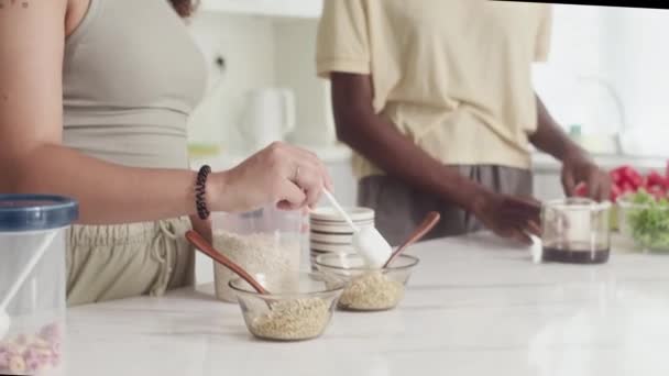 Gekippte Aufnahme von birassischen Freundinnen beim Kochen von Frühstück mit Müsli in der Küche - Filmmaterial, Video