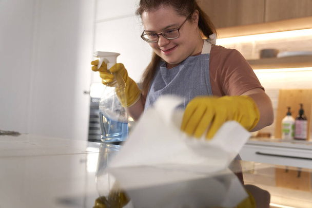 Down syndrome woman cleaning worktop in domestic kitchen - Photo, Image