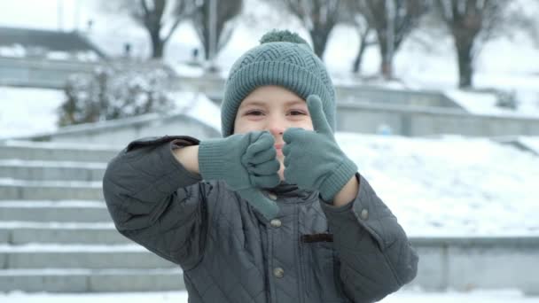 Pequeño niño de invierno mostrando manos gesto pulgares hacia arriba y hacia abajo. - Metraje, vídeo