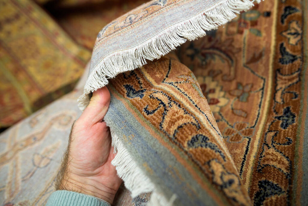 Een persoon is nauw onderzoek van de kleuren en tactiele gevoel van de wol tapijt op de houten parketvloer - Foto, afbeelding