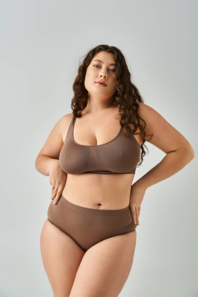 beautiful curvy woman in underwear with curly brown hair looking to camera and posing hands - Zdjęcie, obraz