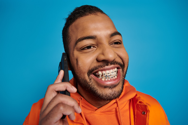 close up of cheerful african american man calling in smartphone against blue background - Φωτογραφία, εικόνα