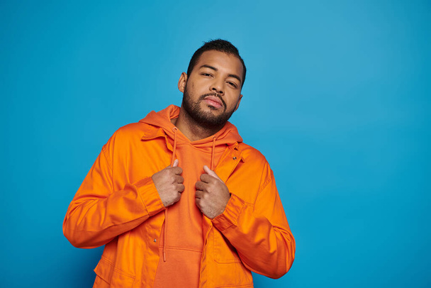 handsome african american young man in orange outfit posing against blue background - Photo, Image
