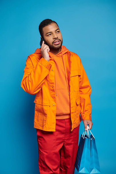 handsome african american guy calling in smartphone and looking to side with shopping bags - Foto, Bild