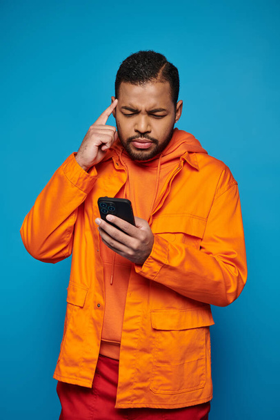 nachdenklicher afrikanisch-amerikanischer Mann in orangefarbenem Outfit scrollt in den sozialen Medien und berührt Tempel - Foto, Bild