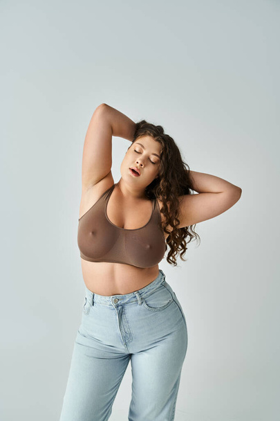 attractive plus size woman in brown bra and blue jeans with closed eyes putting hands behind head - Photo, Image