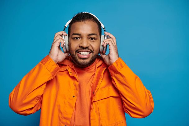 handsome african american man in orange outfit look to camera and hold with hands on headphones - Fotografie, Obrázek