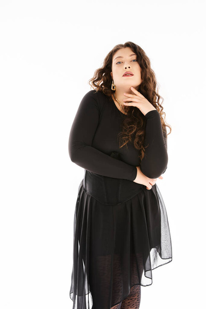 glamourous plus size young woman in black stylish outfit with curly hair and hand on neck posing - Foto, Bild