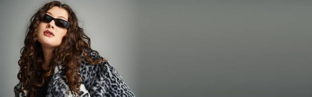 banner di elegante donna plus size in pelliccia di leopardo e occhiali da sole appoggiati in avanti sul grigio - Foto, immagini