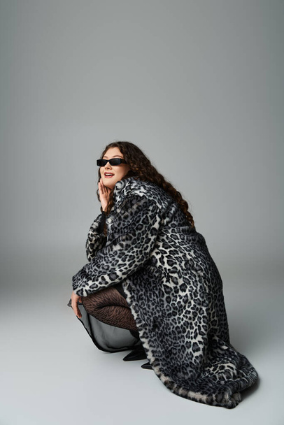 glamourous καμπυλωτή γυναίκα σε γούνα παλτό και γυαλιά ηλίου σκύβοντας προς τα κάτω πλάγια και κοιτάζοντας προς την κάμερα - Φωτογραφία, εικόνα