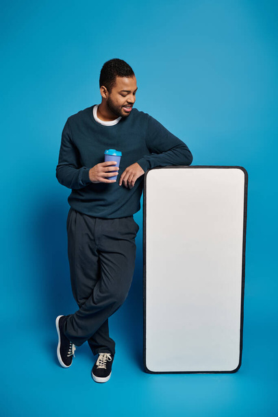 relaxed african american young man holding paper cup and resting near smartphone mockup banner - 写真・画像