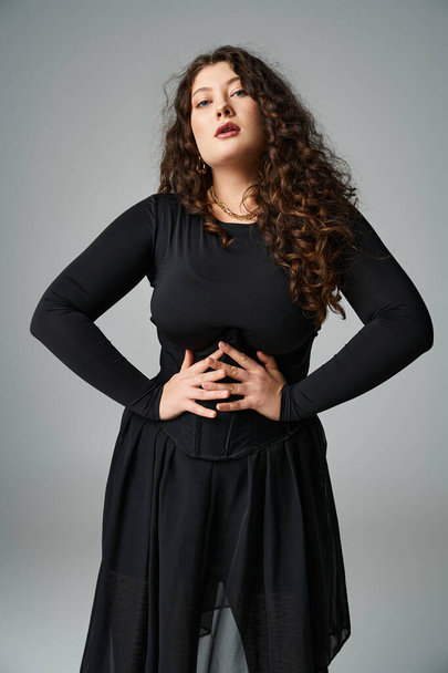 attractive plus size girl looking to camera with hands on waist on grey background - Foto, imagen