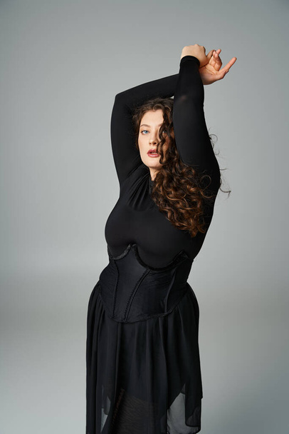 όμορφη καμπυλωτή γυναίκα σε μαύρο κομψό ντύσιμο βάζοντας τα χέρια προς τα πάνω και ψάχνει για πλευρά - Φωτογραφία, εικόνα