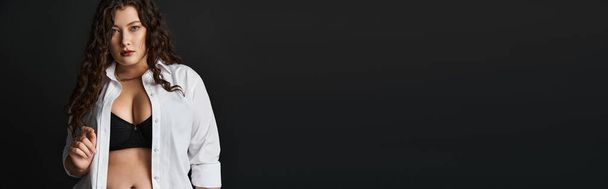 pancarta de mujer de talla grande en camisa blanca, sujetador negro y pantalones con pelo rizado sobre fondo oscuro - Foto, Imagen