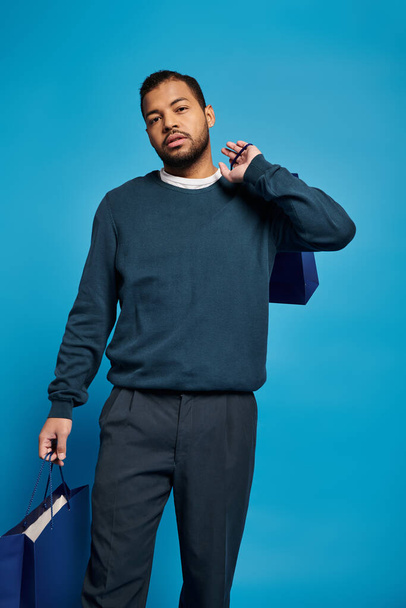 attraente afro americano uomo in abito blu scuro cercando di fotocamera con shopping bags in mano - Foto, immagini