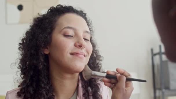 A váll felett a lány használja ecset alkalmazásakor alapítvány arcán többnemzetiségű barátnő piercing az orrban - Felvétel, videó
