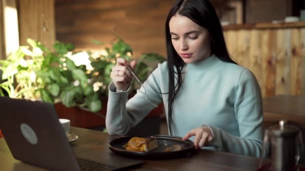 カフェのコンセプトでリラックス. チーズケーキを食べている若い女性. ラップトップコンピュータ付きのテーブル. コピースペース - 映像、動画