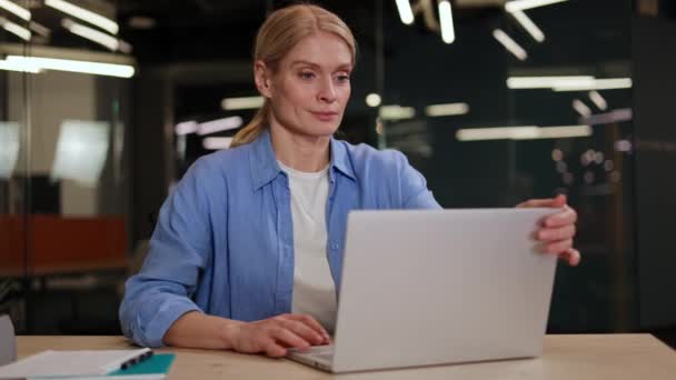 Glimlachende zelfstandige aannemer vrouw klaar met computerwerk rekken en ontspannen tijdens het zitten op de werkplek. Mooie Kaukasische vrouw tevreden door project prestatie en taak gedaan in de tijd. - Video