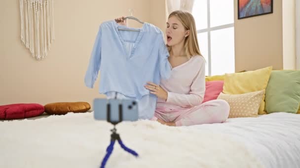 A young woman in pajamas choosing clothing for a vlog in her cozy bedroom with colorful pillows. - Footage, Video