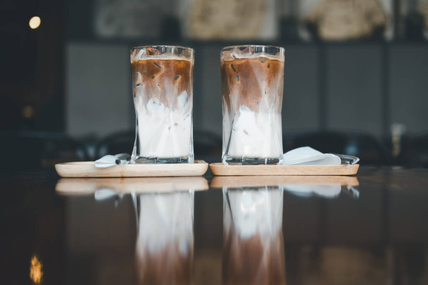 Δύο παγωμένος καφές Mocha δύο στρώσεις φρέσκο γάλα και espresso σύντομο σε ξύλινο τραπέζι στο καφέ. Αναζωογονητικό καλοκαιρινό ποτό, επιλεκτική εστίαση - Φωτογραφία, εικόνα