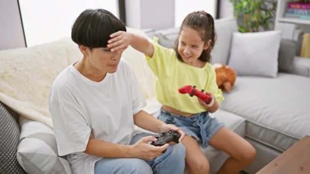 Щаслива мати і дочка сидять на зручному дивані, граючи в відеогру, посміхаючись разом вдома - Кадри, відео