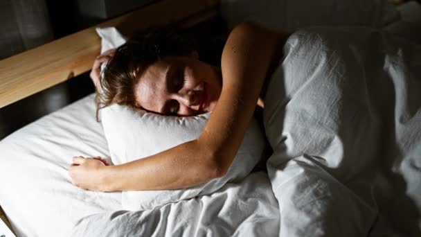 Спокійна молода жінка голосно спить у затишній, тьмяно освітленій спальні, обіймаючи подушку. - Кадри, відео