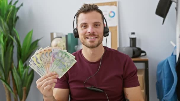 Veselý mladý muž v úřadu, radostně gestikuluje na znamení souhlasu! Oblečený do sluchátek, drží rumunské lei bankovky, vyzařuje z něj pozitivita a úspěch. pohledný chlapík s srdečným úsměvem. - Záběry, video
