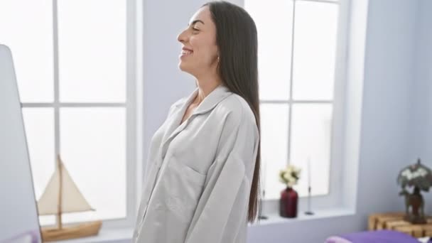 Aanstekelijk gelukkig, jonge Spaanse vrouw expressief glimlachen terwijl comfortabel loungen, volledig ontspannen op haar slaapkamer bed, druipt zelfvertrouwen en genieten van de leuke ochtend vibes - Video