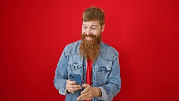 Kendine güvenen genç kızıl saçlı adam, izole edilmiş kırmızı arka planda telefonuyla mutlu bir selfie çekiyor. Gülümsüyor, pozitif enerji ve neşe saçıyor.. - Video, Çekim