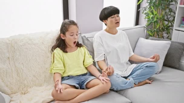 Relaxing at home, mother and daughter bonding over cozy yoga exercise sitting on their comfortable living room sofa - Materiał filmowy, wideo
