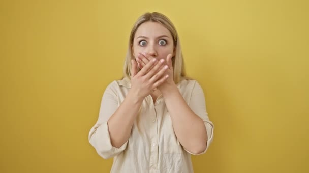 Szőke nő takarja száj sokk, elképesztő hiba szabadult egy meglepetés titkát sárga elszigetelt háttér - Felvétel, videó
