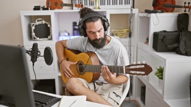 Un giovane barbuto che suona la chitarra al chiuso in uno studio di musica bianca a casa con apparecchiature di registrazione. - Filmati, video