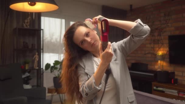 Un video tutorial profesional sobre peinado largo, cabello rizado rebelde con un secador de pelo y cepillo. Una mujer se seca el cabello y hace un volumen basal con un secador de pelo y peine en casa. - Imágenes, Vídeo
