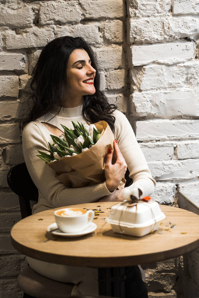 Feliz mulher bebendo café e celebrando aniversário em café com buquê de tulipas e bento cake.Birthday concept.Bento presente bolo - Foto, Imagem