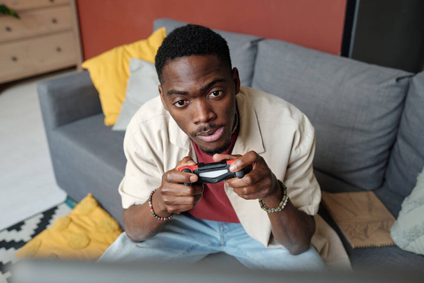 Tenso hombre afroamericano con mando en las manos mirando la pantalla de la computadora durante el videojuego y viendo después de personajes - Foto, imagen