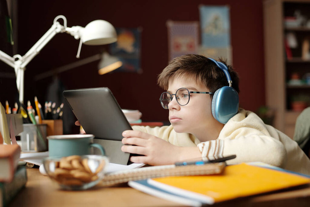 Poważne uczennice w okularach i słuchawkach patrzące na ekran tabletu podczas wykonywania zadania domowego lub oglądania lekcji online - Zdjęcie, obraz